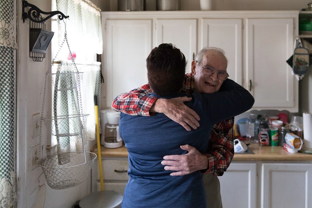 An older gentlemen hugs a woman smiling in his kitchen