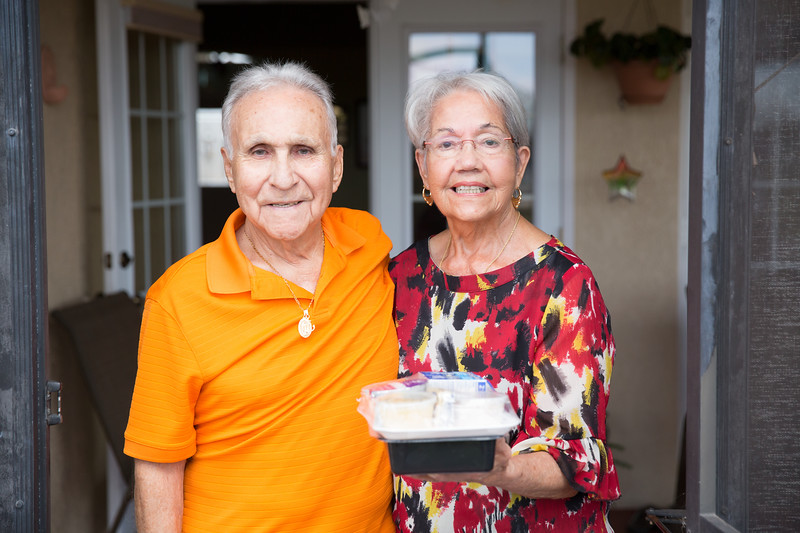 Two older adults standing together doing a Meals on Wheels delivery