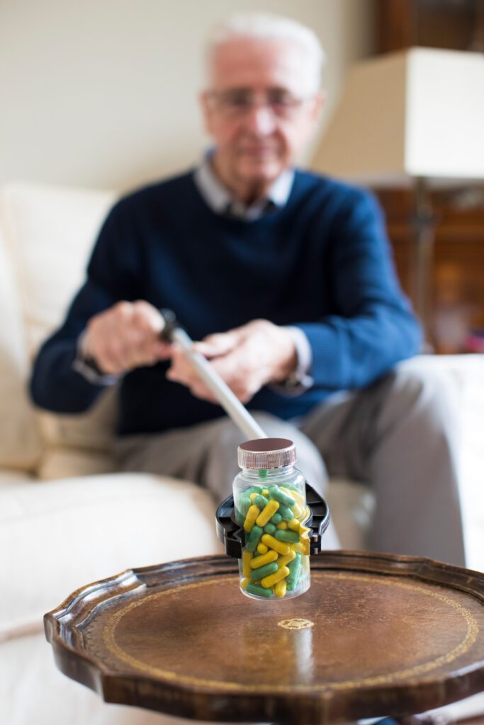 Senior man using reaching arm adaptive technology to pick up medication at home